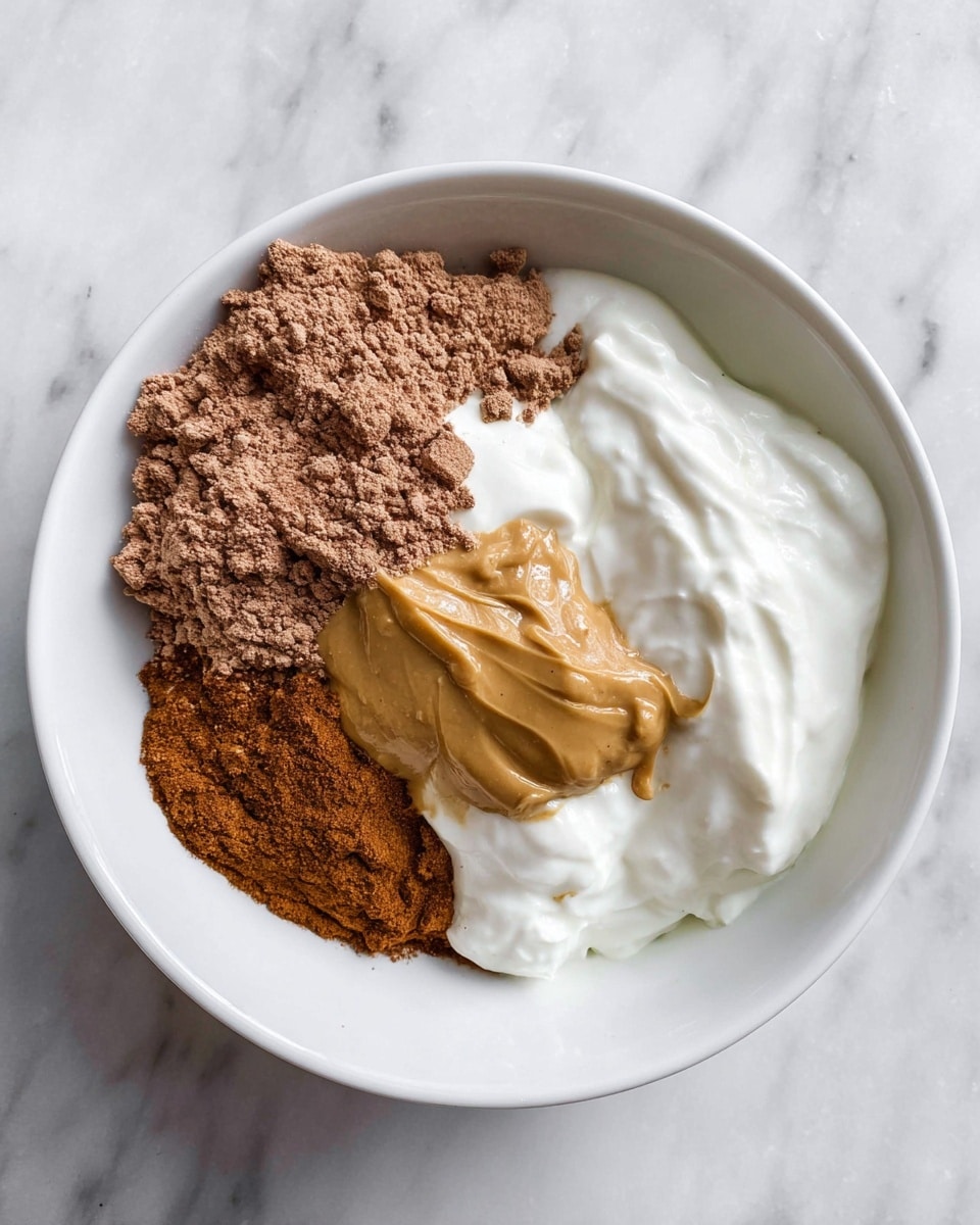 A white bowl sits on a white marbled surface holding four distinct layers: a large scoop of thick white yogurt on the right, a medium dollop of smooth golden-brown peanut butter next to it on the upper side, a light brown powder of cocoa protein on the left side piled high and crumbly, and a fine layer of cinnamon powder in the middle peeking between the yogurt and peanut butter. Each layer is separate and clear in texture and color. photo taken with an iphone --ar 4:5 --v 7