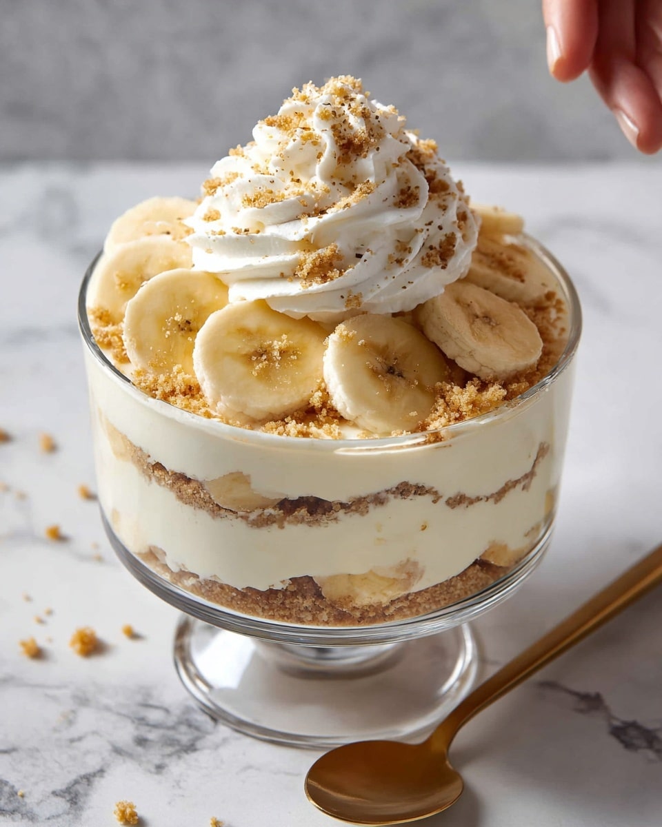 The image shows a clear glass dessert bowl filled with three visible layers: the bottom layer is light brown crushed crumbs, the middle layer is thick, creamy pale yellow pudding, and the top layer is a thick layer of white whipped cream. On top of the whipped cream, there are several banana slices arranged mostly around the edges, with more crumbs sprinkled over the whole top. The bowl sits on a white marbled surface with a golden spoon nearby and extra banana slices scattered around. The scene is softly lit and cozy. Photo taken with an iphone --ar 4:5 --v 7