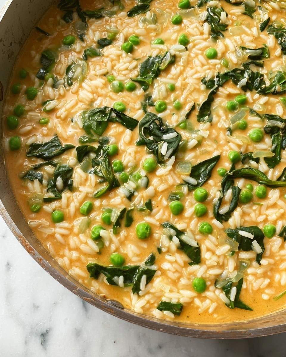A close-up view of a creamy dish in a pan showing three main layers: small pieces of white rice shaped like short grains form the base and fill most of the pan, bright green peas are scattered evenly throughout, and dark green leafy vegetables are mixed in between. The whole dish is covered in a light orange creamy sauce that gives a smooth and rich texture, with some light translucent pieces of onion visible. The pan rests on a white marbled surface. photo taken with an iphone --ar 4:5 --v 7