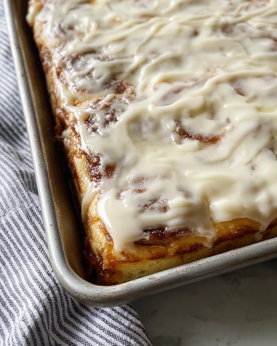 The image shows a close-up of a rectangular bakery tray filled with a layered cinnamon roll sheet cake. The bottom layer is a golden-brown baked dough, topped with a sticky cinnamon-sugar layer that has slightly caramelized around the edges. On top, there is a thick coating of white, creamy icing that is melting slightly, covering the surface unevenly and revealing some cinnamon spots underneath. The tray rests on a white marbled textured surface with a striped cloth visible at the side. Photo taken with an iphone --ar 4:5 --v 7