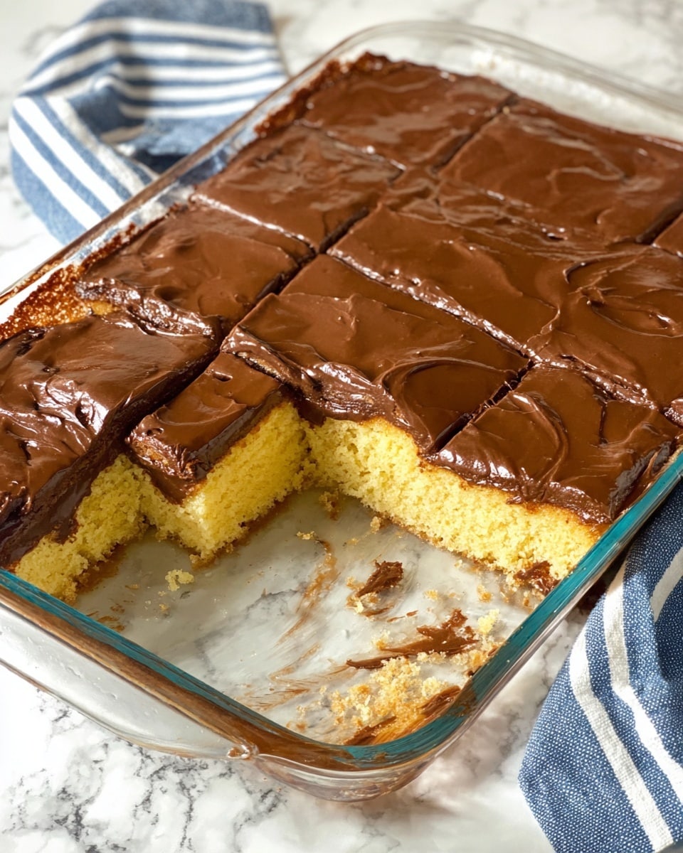 This image shows a rectangular glass dish with a partially eaten layered dessert. The dessert has two layers: the bottom layer is a light yellow cake with a soft texture, and the top layer is a thick, smooth, dark brown chocolate frosting with a slightly shiny surface. Several squares have been cut out from the dish, revealing the clean, even layers. The dish is placed on a white marbled surface with a striped blue and white cloth nearby. Photo taken with an iphone --ar 4:5 --v 7