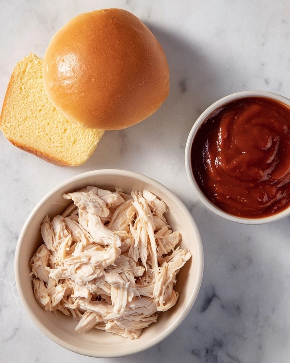 A white bowl filled with torn pieces of light beige cooked chicken sits near the bottom left. At the top left, there is a shiny golden brown sandwich bun with one half resting on the other with a soft yellow inside visible. On the right side, a white round bowl contains smooth, thick reddish barbecue sauce. All items are placed on a white marbled surface. Photo taken with an iphone --ar 4:5 --v 7