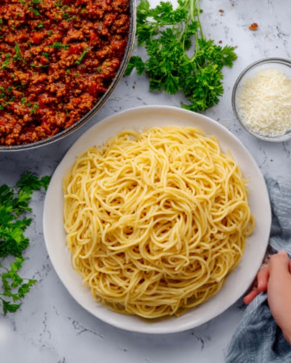 A white plate filled with a nest of plain cooked spaghetti pasta that forms a dense, light golden-yellow mound with a smooth texture. To the top left, there is a pan containing rich, red meat sauce with visible small chunks of meat and herbs, surrounded by sprigs of fresh green parsley on a white marbled surface. In the middle background, there is a small clear container with white grated cheese. A woman's hand is reaching from the right side towards the white plate. Photo taken with an iphone --ar 4:5 --v 7