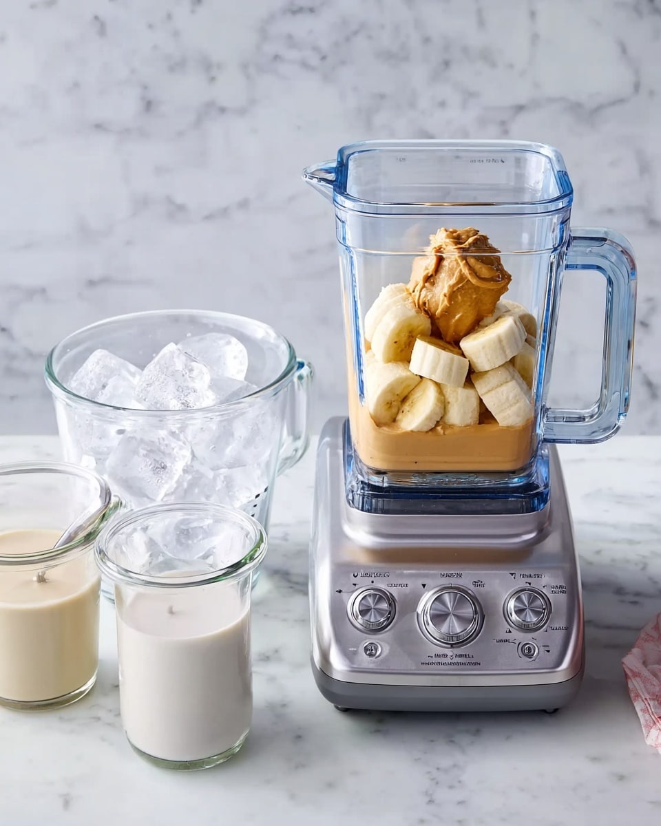 The image shows a blender container with several thick banana pieces and a dollop of light brown peanut butter on top, placed on a silver blender base with buttons and a dial. To the left, there are two clear glass measuring cups on a white marbled surface: one filled with ice cubes and the other filled with a creamy white liquid. The scene is clean and bright with a white marbled background. photo taken with an iphone --ar 4:5 --v 7