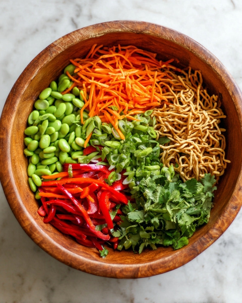 A wooden bowl filled with six colorful sections arranged side by side inside: bright green edamame, shredded orange carrots, sliced green onions, bright red bell pepper strips, fresh green cilantro leaves, and light brown crunchy noodles. The bowl sits on a white marbled surface. photo taken with an iphone --ar 4:5 --v 7