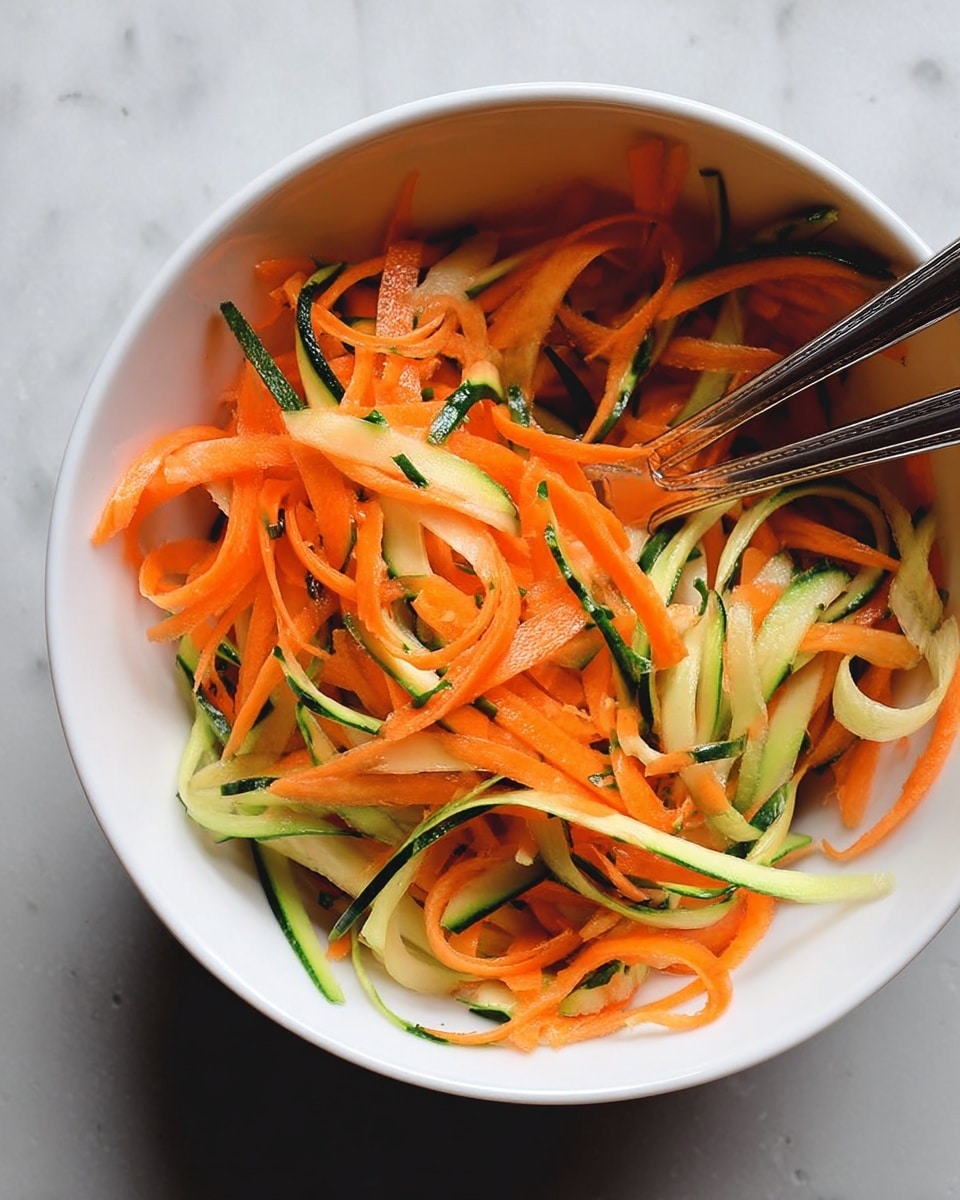 A white bowl filled with thin, long strips of bright orange carrot and green cucumber mixed together, showing a fresh and crunchy texture. The carrot strips are thin and slightly curly, while the cucumber strips have a darker green skin on one side and pale green inner flesh, both intertwining naturally. Two silver forks rest inside the bowl on opposite sides, partially buried in the veggie strips. The bowl is set on a white marbled surface. photo taken with an iphone --ar 4:5 --v 7