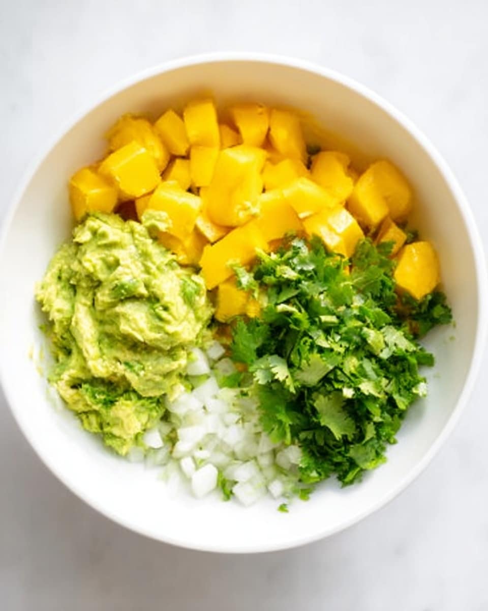 In a white bowl on a white marbled surface, there is a colorful mix of ingredients arranged in separate sections. On the left side, there is a layer of chunky green avocado mash with a creamy texture. Next to it, toward the center, are bright yellow mango cubes that look fresh and juicy. To the right, a pile of finely chopped fresh green cilantro adds a leafy texture. Below the mango and cilantro, small white onion pieces give a crisp contrast. The ingredients are cleanly separated but close together in the bowl, ready to be mixed. photo taken with an iphone --ar 4:5 --v 7